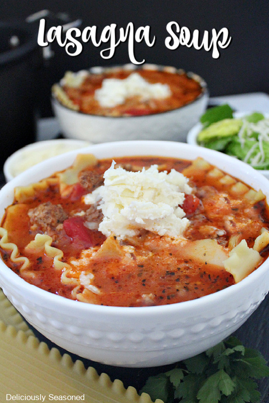 Two white bowls filled with Lasagna Soup with a small side salad and extra cheese mixture in the background.