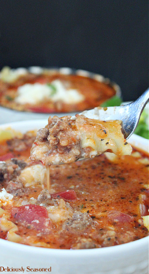 A spoonful of lasagna soup being held above the bowl full of soup with a white bowl of soup in the background.