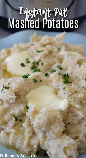 A light blue bowl filled with mashed potatoes with butter that has started to melt, topped with a little parsley flakes.