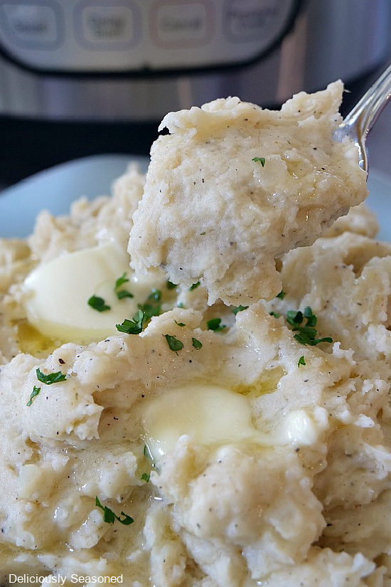 A light blue bowl filled with mashed potatoes with a heaping spoonful of potatoes being shown.