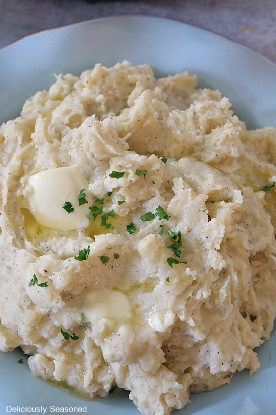 A light blue bowl filled with Instant Pot Mashed Potatoes with butter that has started to melt, garnished with parsley flakes.