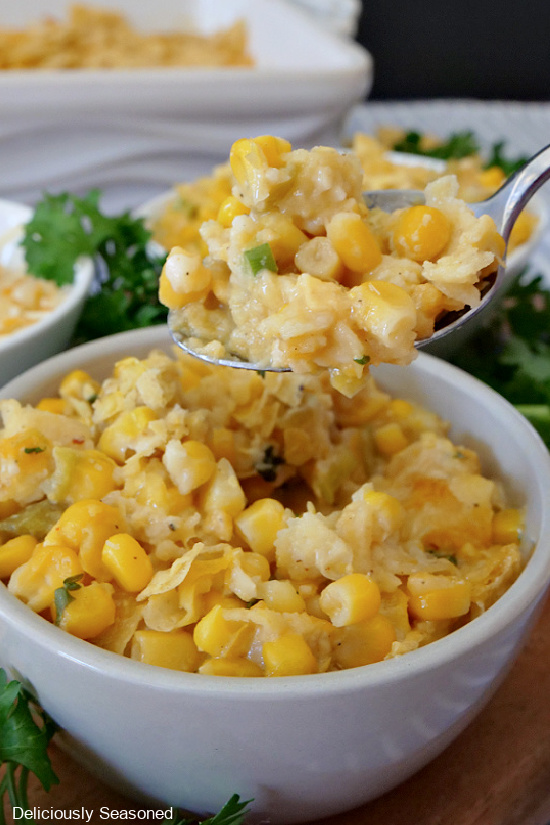 A light grey bowl with green chili corn casserole and a spoonful of corn casserole being held up above the bowl.