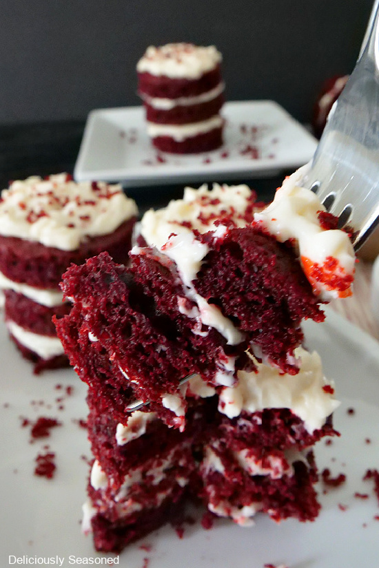 A close up view of a bite of mini red velvet cake on a fork with two other mini cakes in the background.