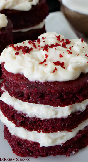 A close up shot of 3 mini red velvet cakes with cream cheese frosting between the layers with cake crumbs on top.