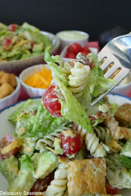 A fork with lettuce, tomato, bacon, pasta on it, showing the salad ingredients.