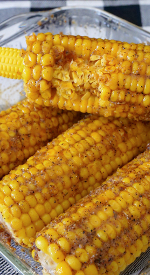 A close up shot of 4 Cajun buttered corn on the cob with one bite taken out of one of the ears of corn.