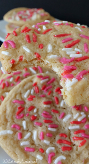A close up picture of a sugar cookie with a bite taken out of it with other sugar cookies on a white plate in the background.