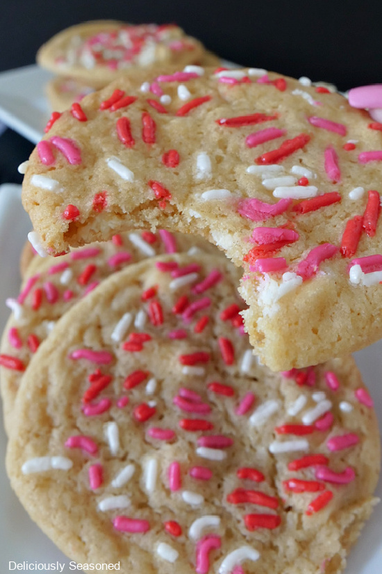 A close up photo of a sugar cookie with red, white, and pink sprinkles on top, with a bite taken out of it.