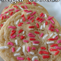 A close up photo of 3 sugar cookies with long pink, white, and red sprinkles on top, laying on a white plate