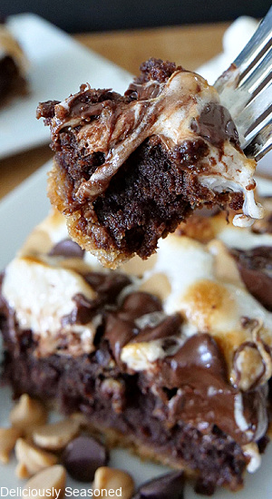 A serving of Peanut Butter S'mores Brownies on a white plate with a bite on a fork being held up above the brownie.
