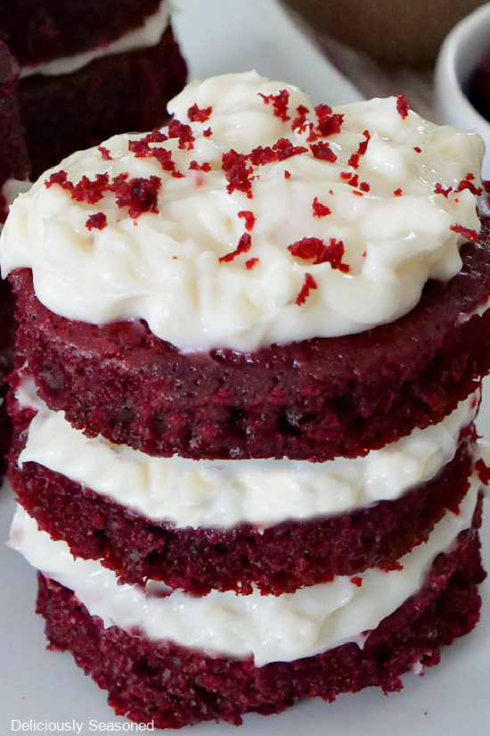 A close up photo of one 3 layer mini red velvet cake with cream cheese frosting between each layer, topped with cake crumbs.