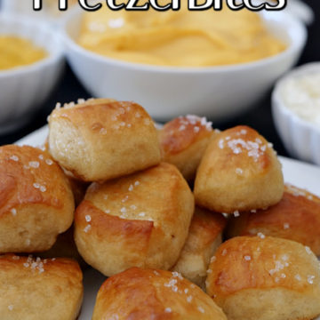 A stack of soft pretzel bites on a white plate with three small bowls with dipping sauces in the background.