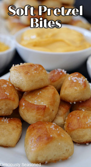 A close up picture of Soft Pretzel Bites on a white plate with mustard, nacho cheese, and cream cheese in white bowls in the background. The title is centered at the top of the picture. 