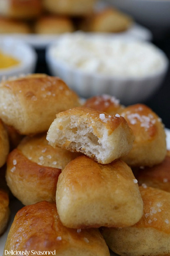 A stack of soft pretzel bites piled high with the top pretzel with a bite taken out to show the soft center.