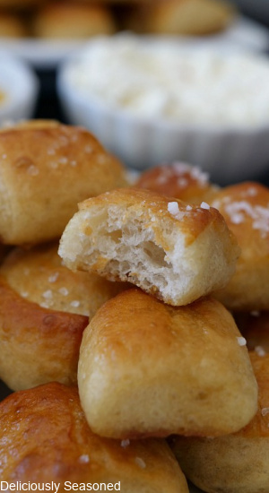 A close up picture of Soft Pretzel Bites stacked on top of one another with a bite taken out of the top pretzel bite, showcasing the soft and chewy inside. 