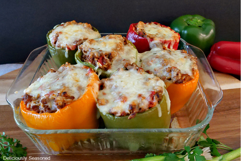 A baking dish filled with 6 stuffed bell peppers sitting on a wood cutting board.