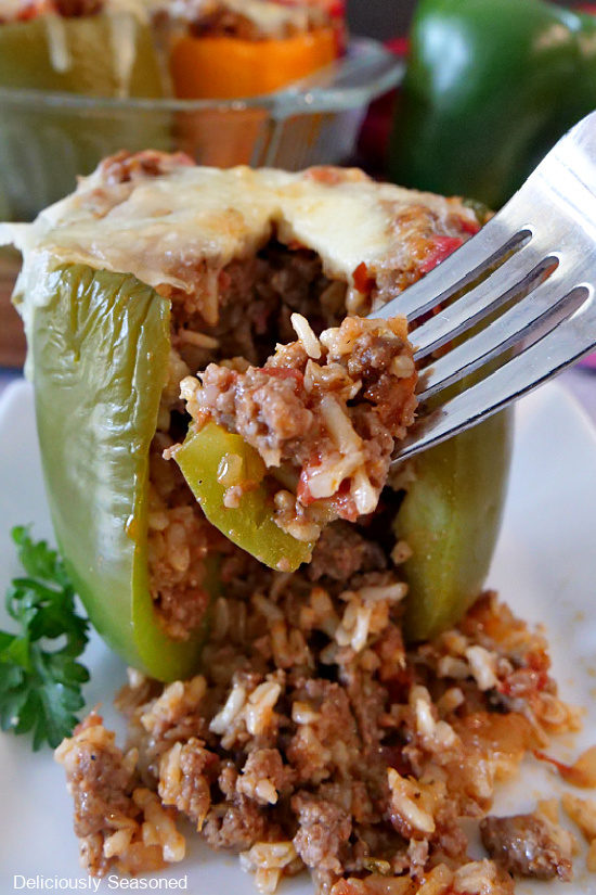 A bite of stuffed bell peppers with the whole green bell pepper in the background sitting on a white plate.
