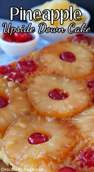 A pineapple upside down cake with pineapple rings and cherries on top of it with 2 small white bowls in the background filled with cherries and pineapples.