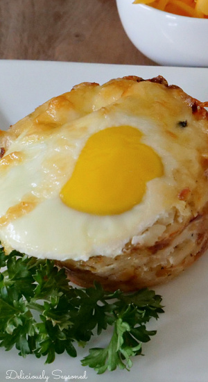 A close up photo of a hash brown breakfast cup on a white plate with parsley in the forefront. 