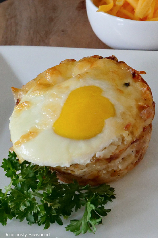 A close up photo of hash brown breakfast cups on a white plate with parsley for decoration.
