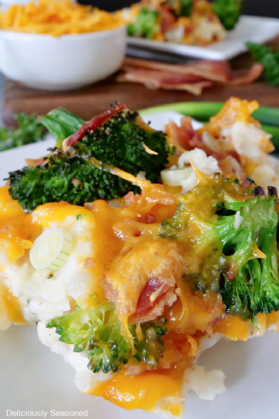 A white plate with a close up picture of broccoli mashed potato bake showing the broccoli, cheese, green onions, bacon and mashed potatoes.