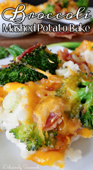 A close up photo of broccoli mashed potato bake on a white plate, topped with melted cheddar cheese and bits of bacon with a small white bowl of cheddar cheese, 2 strips of bacon, and a white plate in the background.