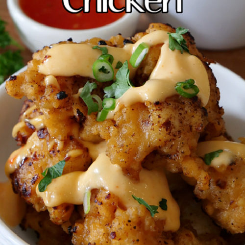 A white bowl filled with Bang Bang chicken bites with a creamy sauce drizzled over the top.