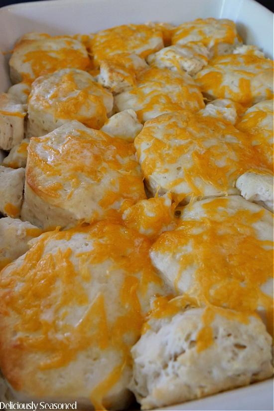 A baking dish filled with golden biscuits topped with melted cheese.