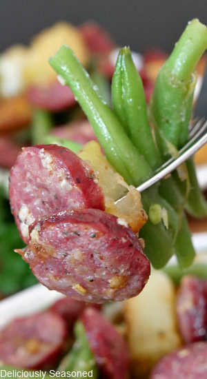 A close up photo of green beans, sausage, and potatoes on a fork.