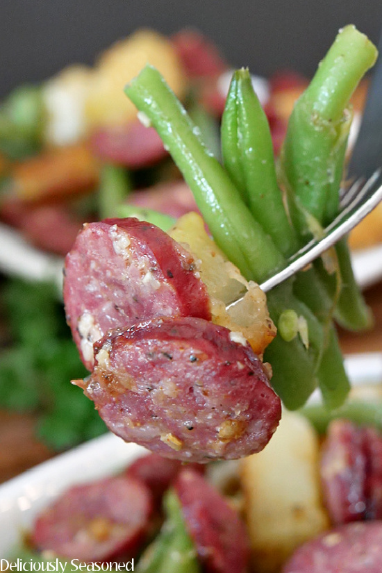 A close up photo of a fork with a bite of potatoes and green beans with sausage.