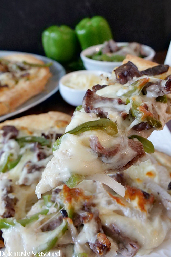 A close up photo of a slice of Philly cheesesteak pizza, topped with mozzarella cheese, onions, beef, and green bell peppers.