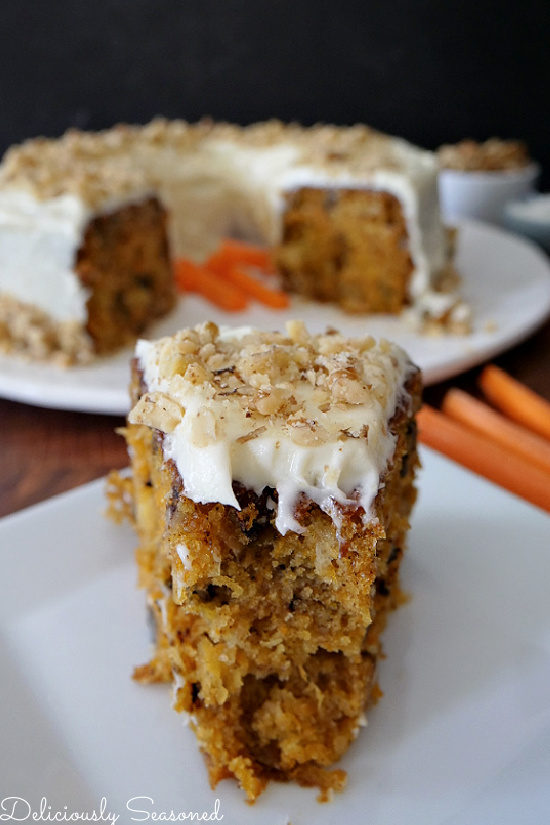 A slice of carrot cake with a bite taken out of it with the whole cake in the background.