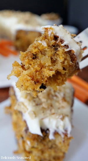 A close up bite of carrot cake with cream cheese frosting on a fork.