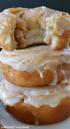 A close up photo of 3honey buns stacked on one another, sitting on a white plate with a bite taken out of the top one.