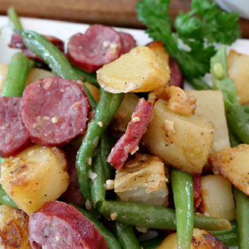 Sausage green beans and potatoes on a white plate.