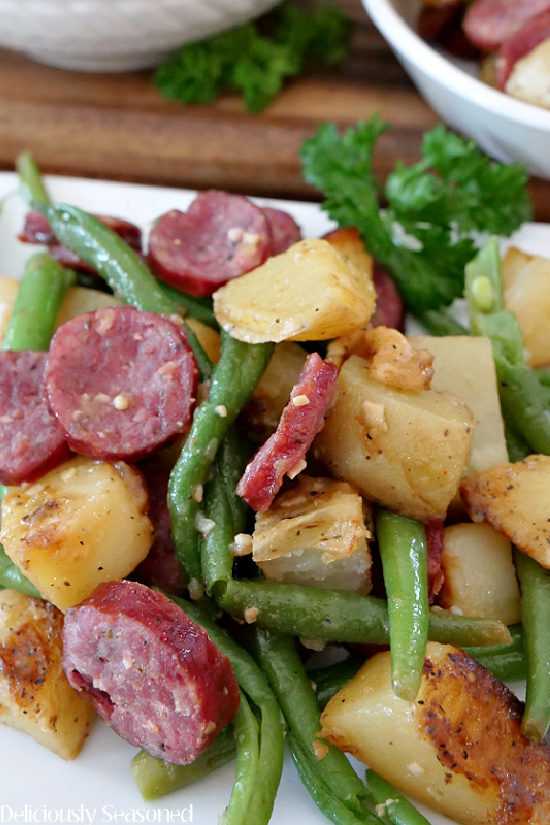 A white plate with potatoes and green beans with sausage on it.