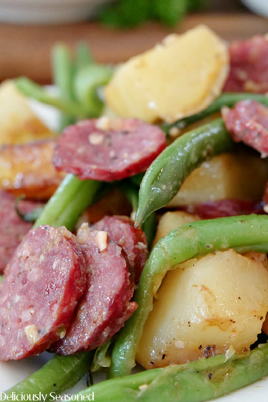 A close up photo of potatoes and green beans with sausage.