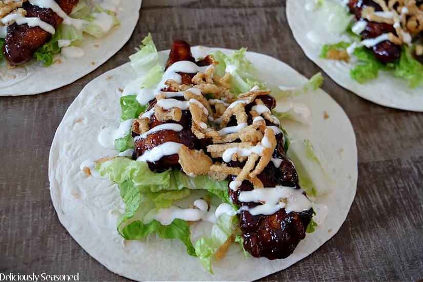 Three honey BBQ chicken wraps that are laying flat on a wood board showing the ingredients.