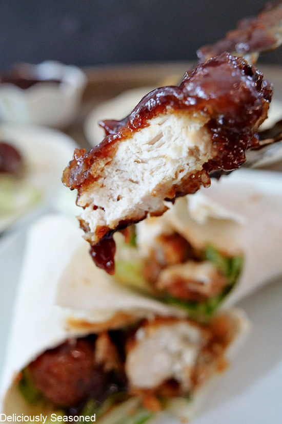 A super close up photo of a piece of chicken covered in honey BBQ sauce with a bite taken out of it.