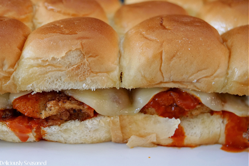 Buffalo Chicken Sliders on a white plate before they are separated, showing the chicken, cheese and sauce between Hawaiian rolls.