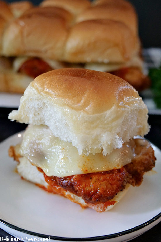 A close up photo of a single buffalo chicken slider on a white plate with black trim.