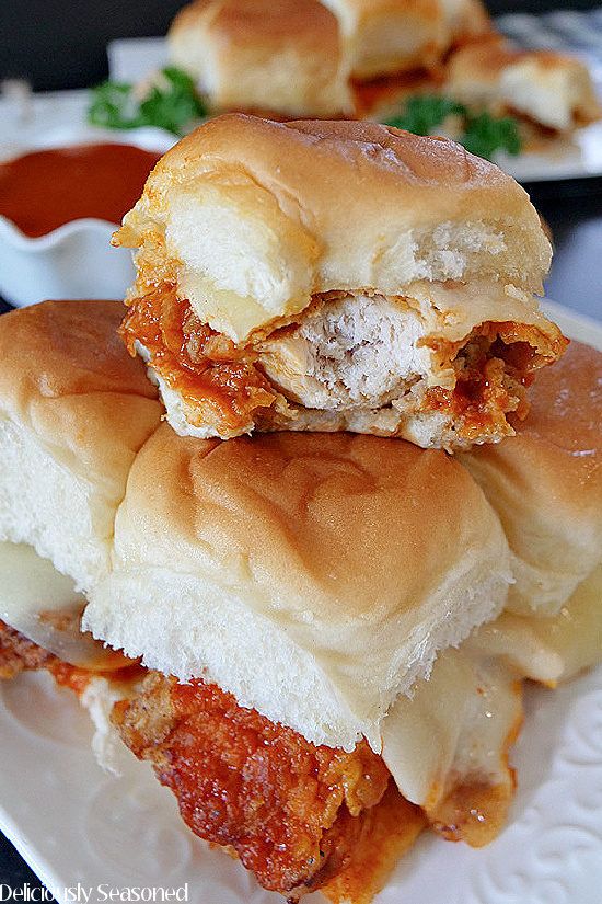 A close up of a buffalo chicken slider with a bite taken out of it, then placed on top of 4 more sliders.