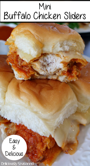 A close up of buffalo chicken slider with a bite taken out of it placed on top of more sliders.