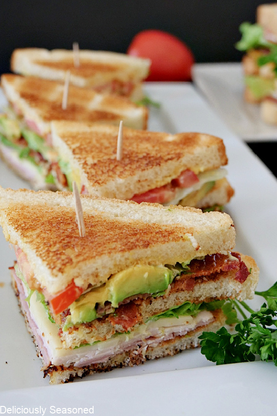 Club sandwiches cut into quarters and lined up on a long white plate.