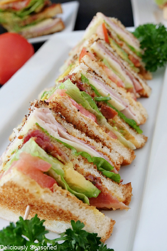 Club sandwiches cut into quarters and laid on their side on a long white plate.