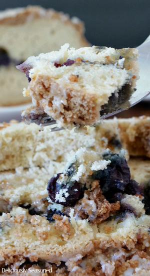 A bite of Blueberry Streusel Cake on a fork being held up above the slice of cake.