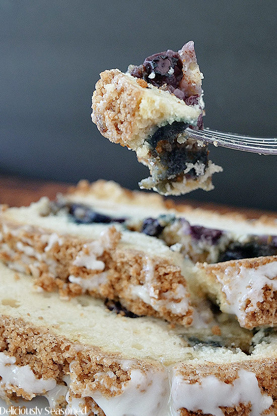 Two slices of Blueberry Streusel Cake placed on a white plate with a fork holding up a bite of the cake.
