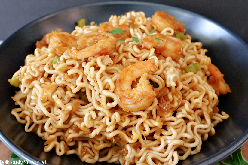 A photo of shrimp chow mein in a black bowl showing the ramen noodles and shrimp on top.