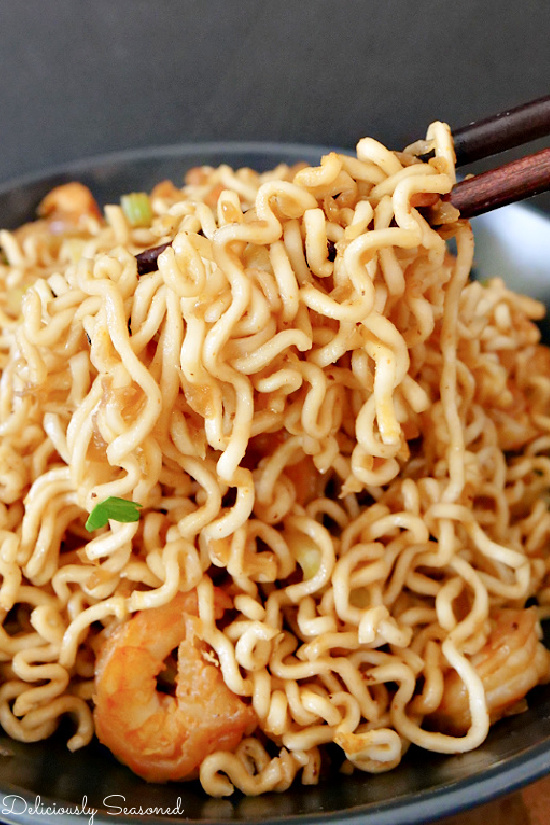 A close up of shrimp chow mein noodles with shrimp being picked up with chopsticks.