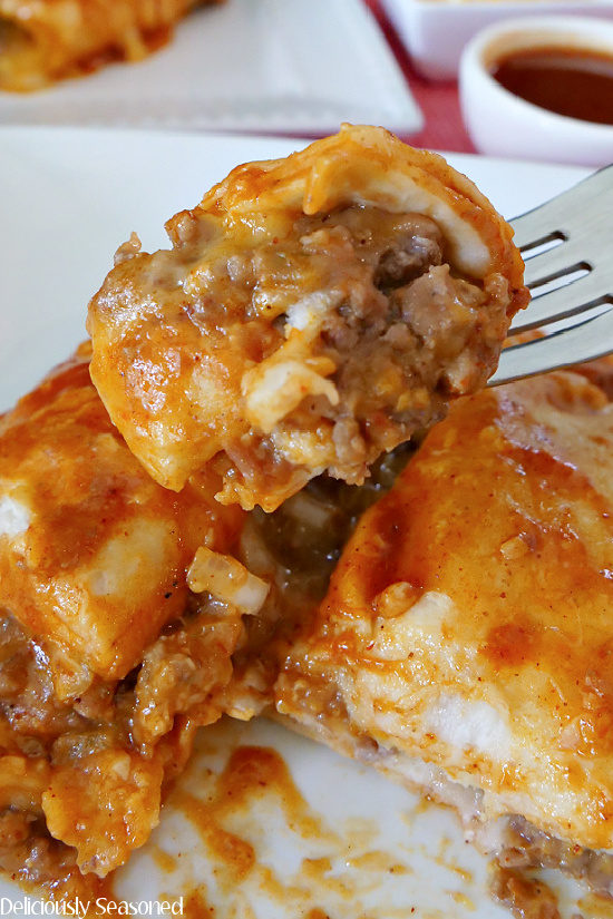 A super closeup photo of a bite of easy beef and cheese enchiladas on a fork held above the two enchiladas on the white plate.